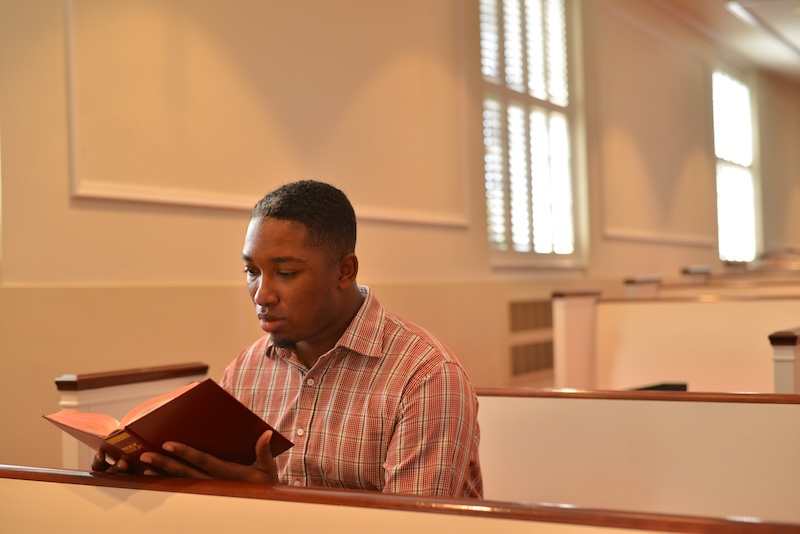 Student in church sitting in a pew and reading